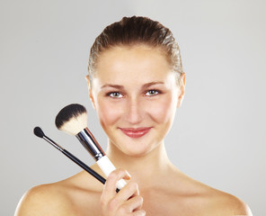 Beautiful young woman smiling holds the make-up brushes