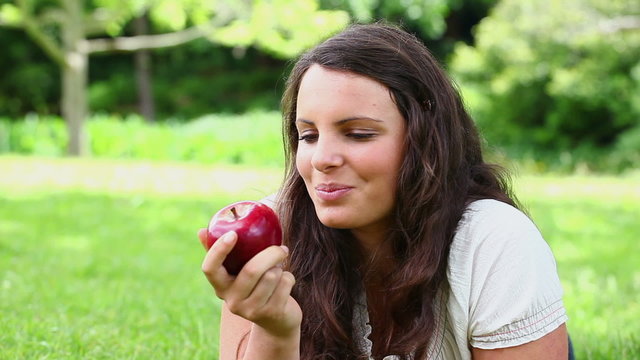 Smiling brunette haired woman eating a red apple