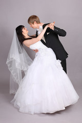Groom and beautiful bride dance in studio on gray background