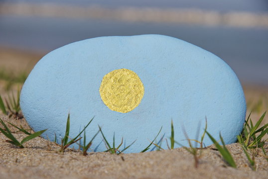 colours of the Palau flag on a stone over the sand
