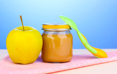 Jar of baby puree with spoon on napkin on blue background
