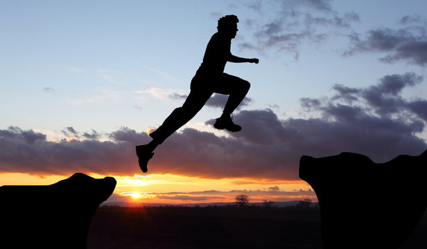 Silhouette of hiking man jumping over the mountains at sunset