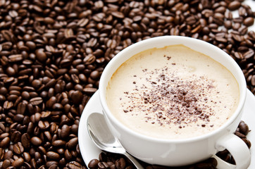 Cup of cappuccino sitting on a pile of coffe beans