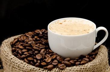 Cup of cappucino sitting on a bag with coffeebeans