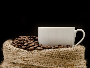 Cup of cappucino sitting on a bag with coffeebeans
