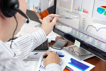 Man on a phone analyzing financial data on computer