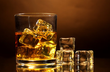 glass of whiskey and ice on brown background