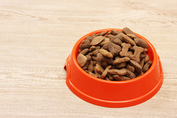 dry dog food in orange bowl on wooden background