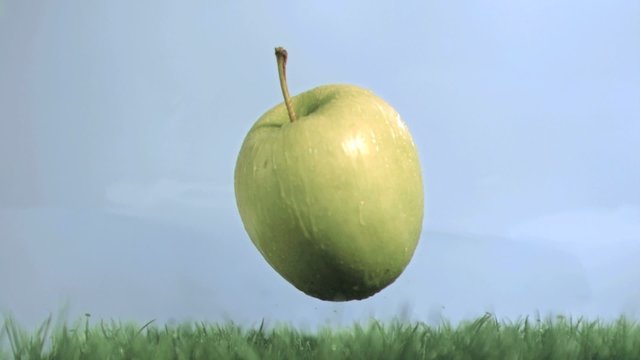 Green apple in super slow motion falling on the grass
