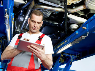 Motor mechanic works under the service lift with his touchpad