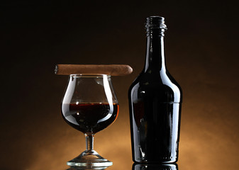 bottle and glass of brandy and cigar on brown background