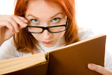 Beautiful red-haired girl in glasses reads book.
