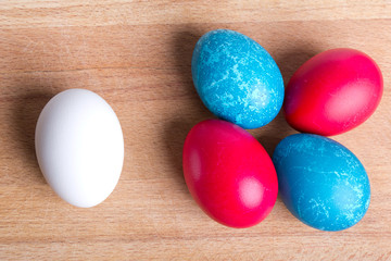 Four colored Easter eggs and white, on a piece of wood