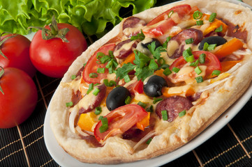 Closeup of pizza with tomatoes, cheese, black olives and peppers
