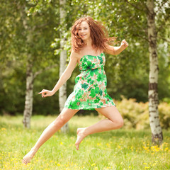 Naklejka na ściany i meble Młoda kobieta rudowłosy skoków w parku z kwiatami