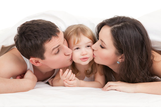 Happy family, mother, father and daughter on the white bed