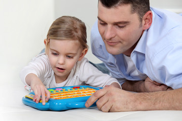 Father watching daughter play with electronic toy - obrazy, fototapety, plakaty