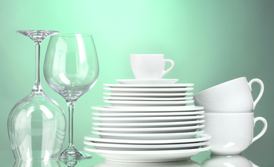 Clean plates, cups and glasses on green background