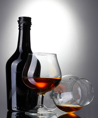 Glasses of brandy and bottle on gray background
