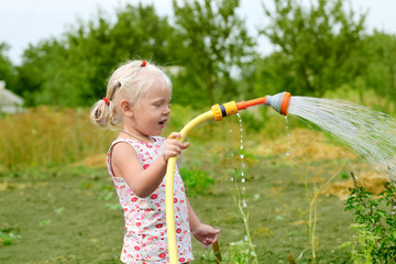 Little girl watering the grass in the garden