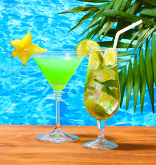 Glasses of cocktails on wooden table on blue sea background