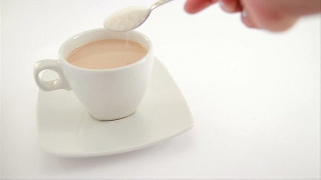 adding sugar to a cup of coffee and milk