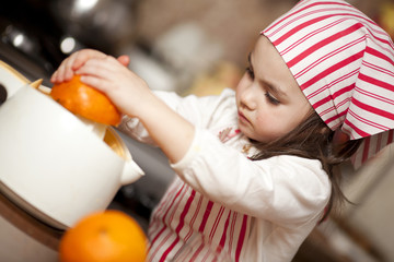 Little girl making fresh and healthy orange juice with kitchen a