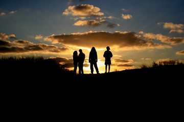 Fototapeta na wymiar silhouette of friends standing on dune in sunset