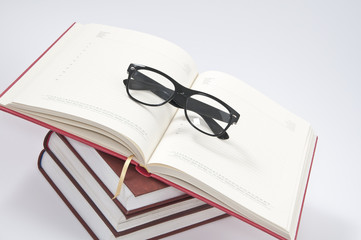 Stack of books with opened notebook and glasses