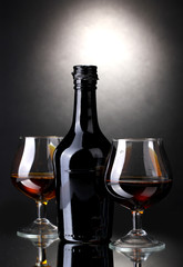 Glasses of brandy and bottle on gray background