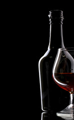 Glass of brandy and bottle on black background