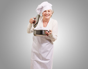 portrait of cook senior woman opening sauce pan over grey