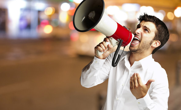 portrait of young man shouting with megaphone at city by night