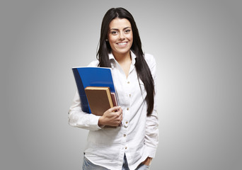 young student holding books and smiling against a grey backgroun