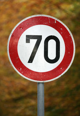Ein Tempo 70 Schild vor herbstlichem Wald