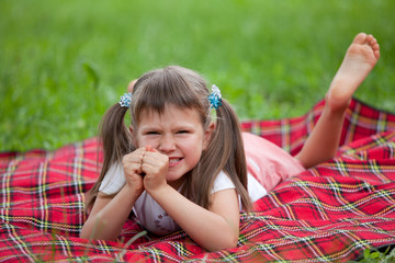 Little irritated girl preschooler lying on plaid and grass