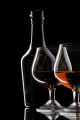 Glasses of brandy and bottle on black background
