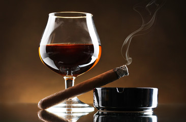 glass of brandy and cigar on brown background