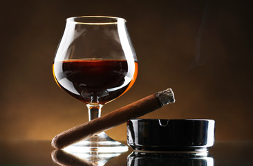 glass of brandy and cigar on brown background