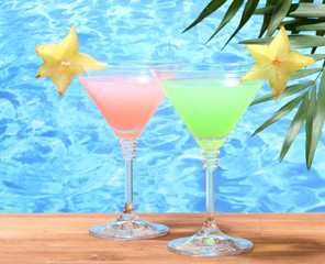 Glasses of cocktails on wooden table on blue sea background