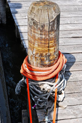 Naklejka premium an orange rope wrapped around a timber stump at a shipping pier