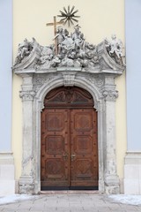 Fototapeta na wymiar Entrance to a church. Wooden door, stone statuettes above it.