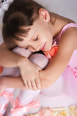 The small tired ballerina sits on a floor in rose-petals