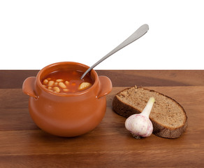 Soup in clay pot with bread and garlic on wooden table