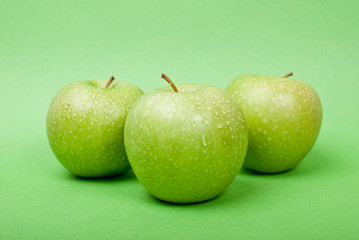 Ripe green apples with water drops on green background
