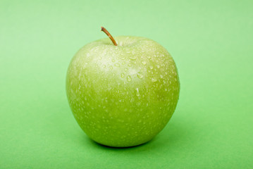 Ripe green apple with water drops on green background
