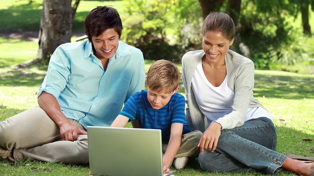 Happy family looking at a laptop while sitting on the grass