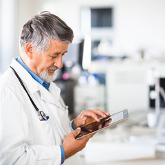 Senior doctor using his tablet computer at work (color toned ima