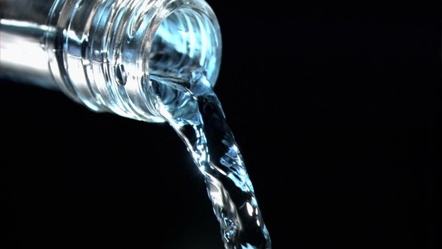 Close up, trickle of water in a super slow motion flowing of the glass bottleneck with blue reflexio