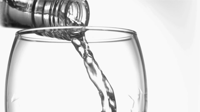 Trickle of water in a super slow motion flowing of the glass bottleneck in a tumbler glass